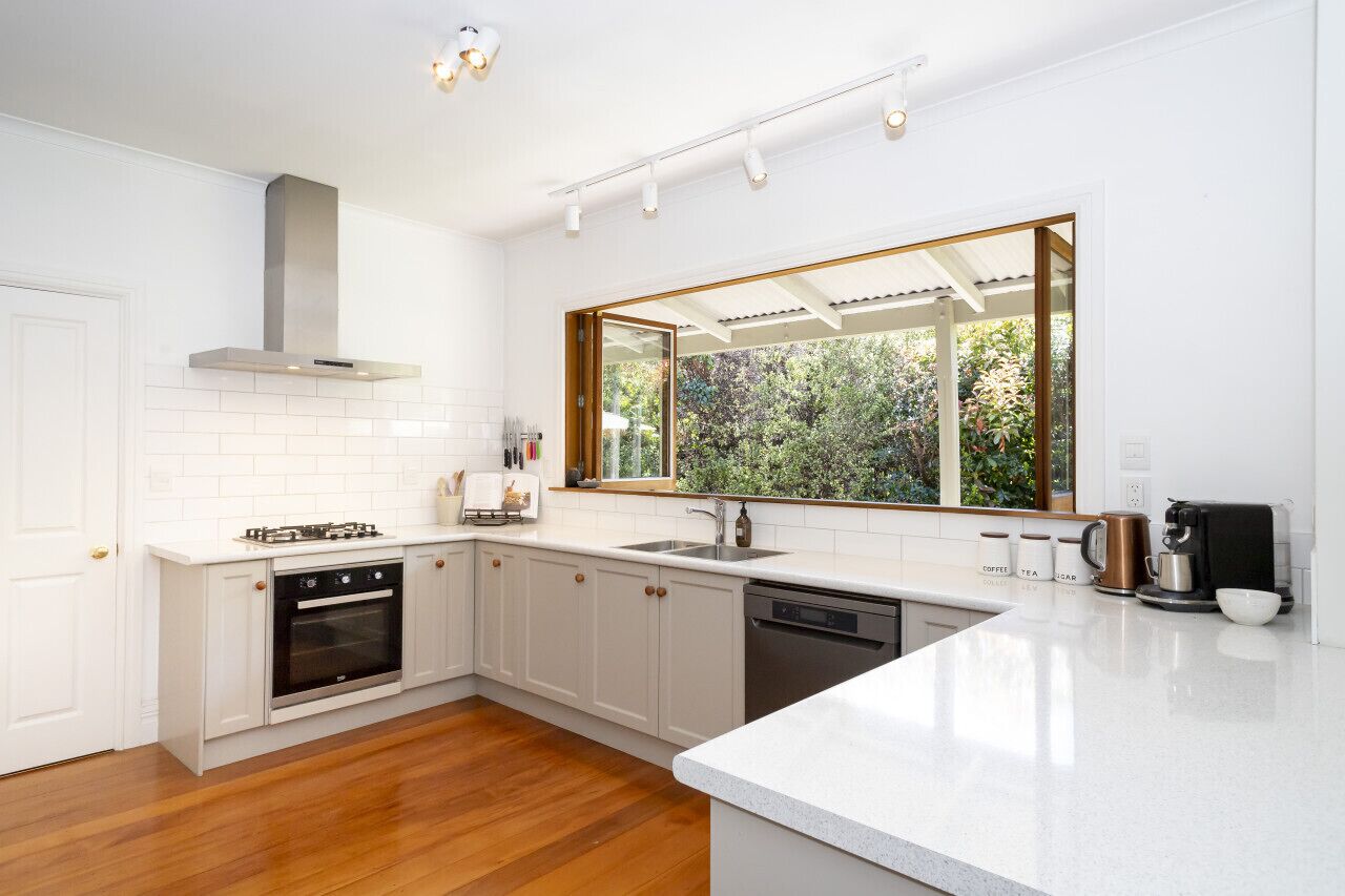 A modern kitchen with white cabinetry, a large window, and a built-in oven and dishwasher.