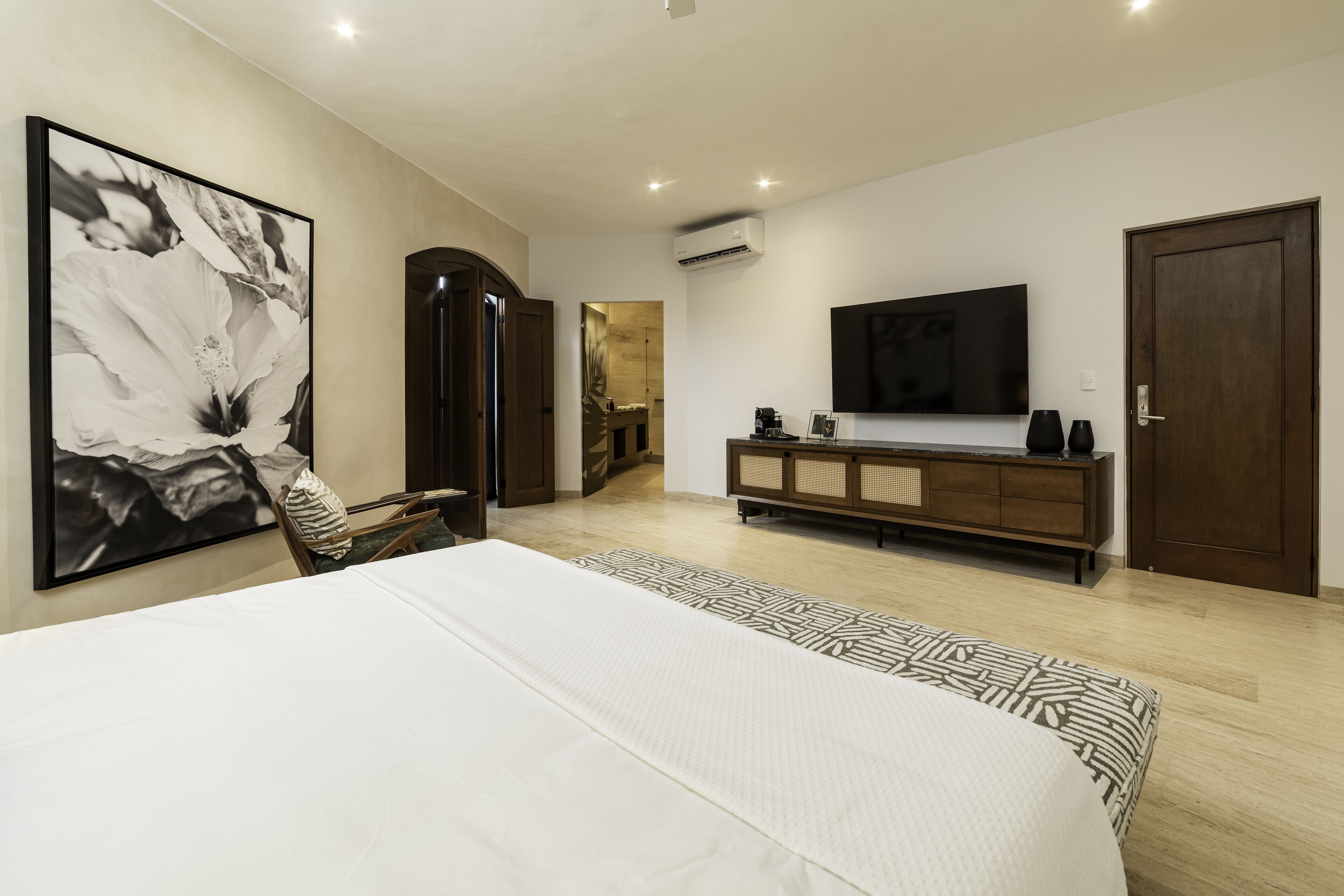 Ein Schlafzimmer mit einem großen Bett, einem an der Wand montierten Fernseher, einem Holzschrank und einer Tür.
