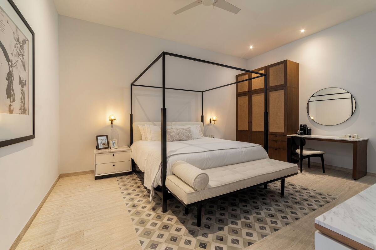 Een slaapkamer met een hemelbed, een bureau met stoel, een garderobe en een nachtkastje met lamp.