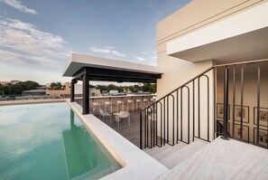 Un área de piscina en la azotea con un espacio de estar techado y una escalera que sube a un nivel superior.