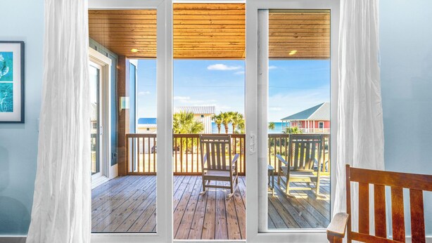 Ein Zimmer mit einer Holterrasse, einem Schaukelstuhl und Blick auf Strand und Gebäude.