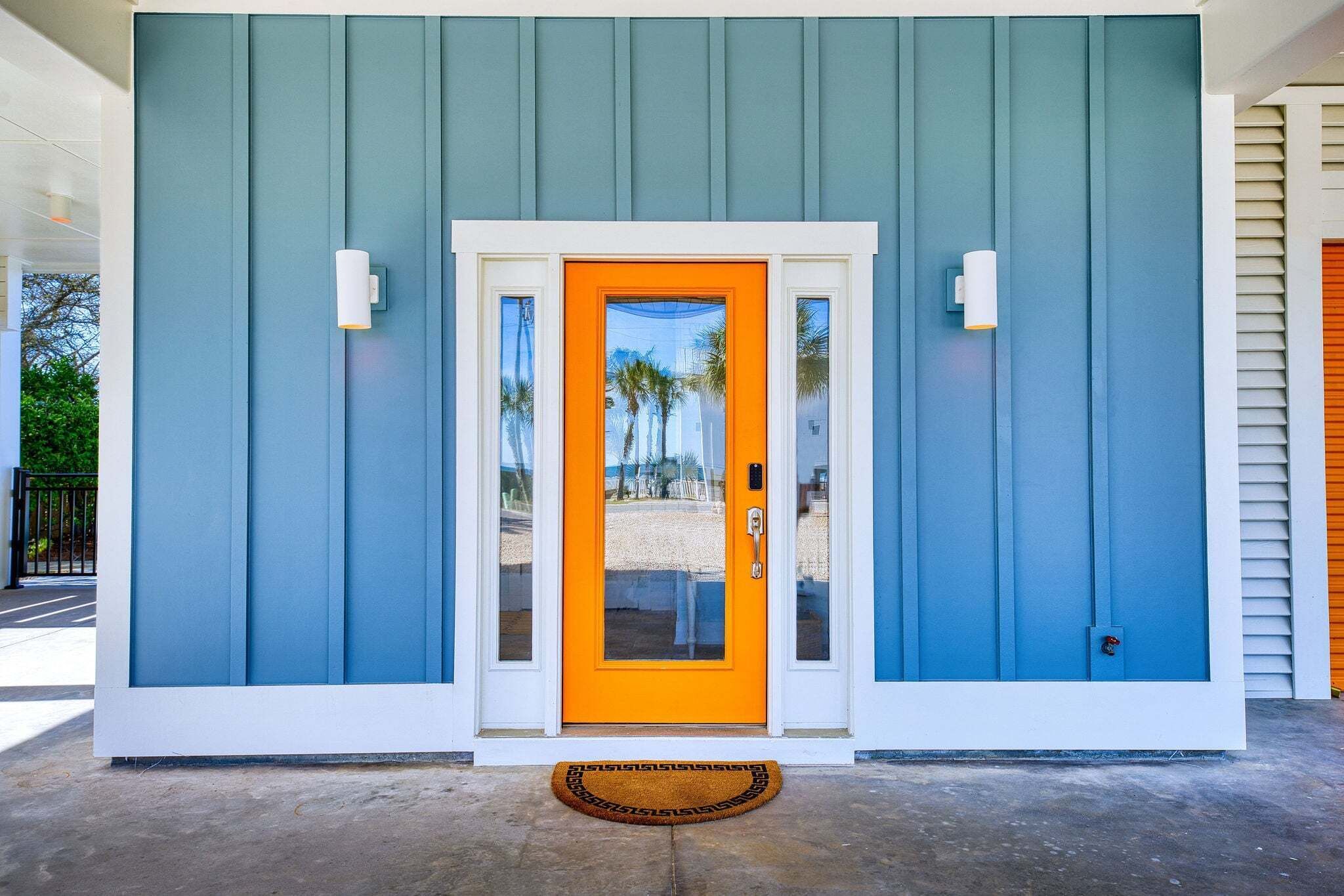 A building with a blue exterior, a bright orange door, and a small porch area.