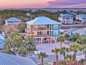 Une maison à plusieurs étages située en bord de mer, dotée d’un balcon et entourée de palmiers et d’autres immeubles résidentiels.