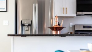 Ett modernt kök med vita skåp, rostfria vitvaror och en kopparkastrull på bänkskivan.