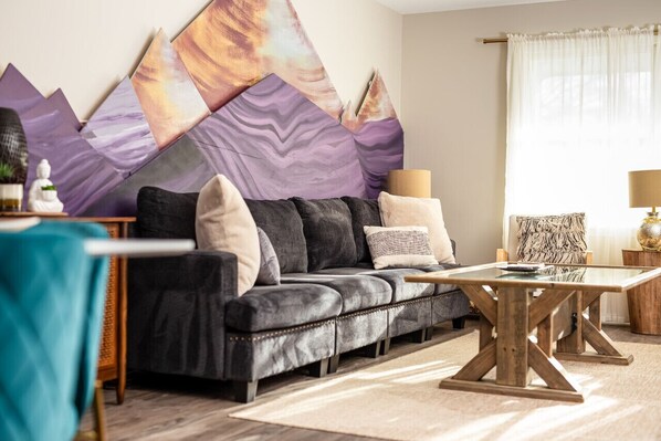 A modern living room with a black leather sofa, a glass coffee table, and a large abstract painting on the wall.