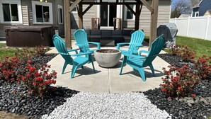 A covered outdoor seating area with Adirondack chairs, a fire pit, and a barbecue grill.