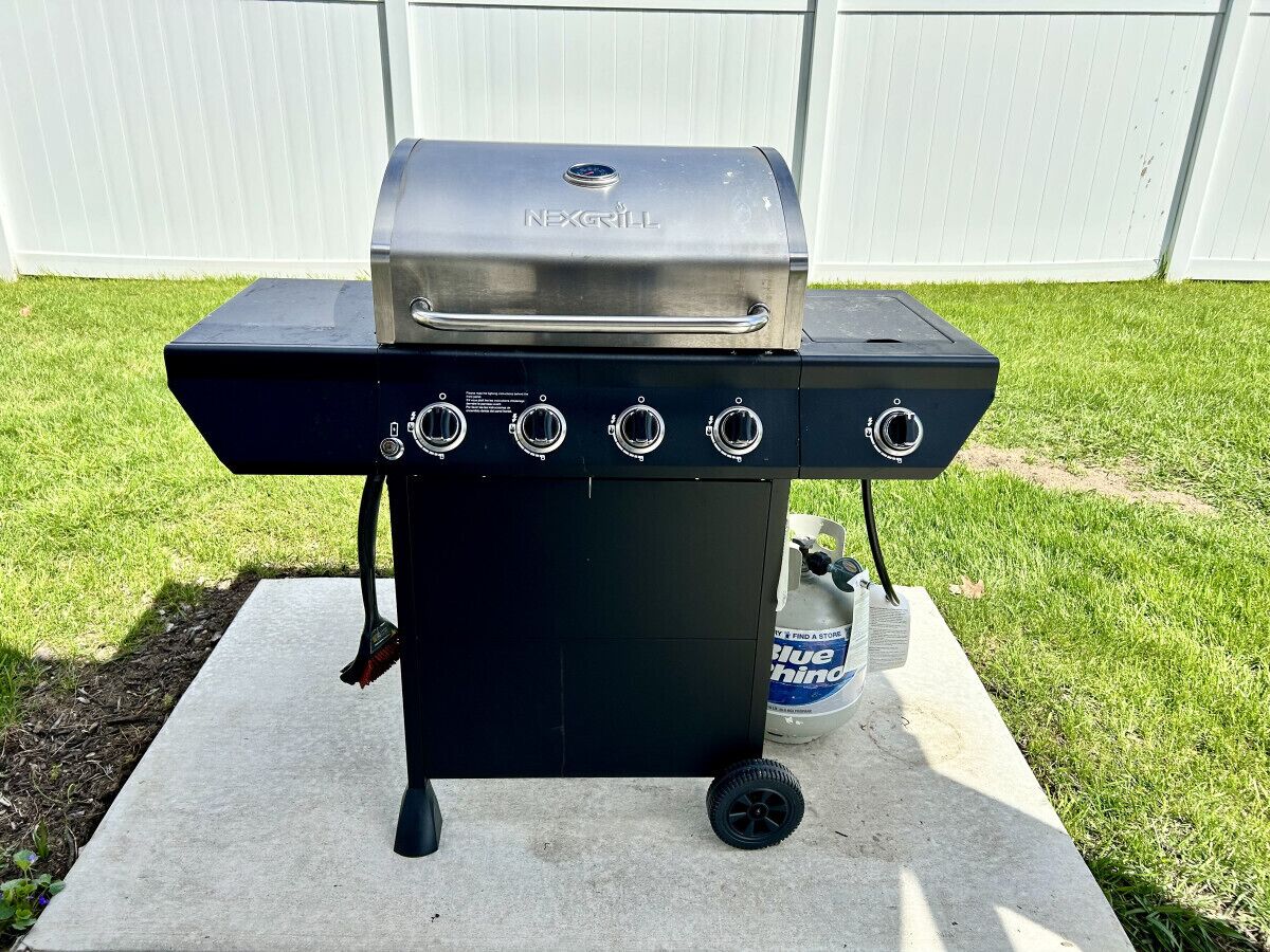 A black outdoor grill with four burners and a digital display, placed on a concrete pad.