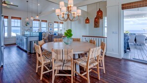 A spacious kitchen with a central island, a dining area with a round table and chairs, and a view of the ocean through large windows. - Sky High • Panoramic Views, Dock Slip, Steps to Tahiti Beach - Hope Town (Hope Town)