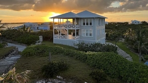 A two-story house with a balcony, surrounded by lush greenery and a view of the sunset. - Sky High • Panoramic Views, Dock Slip, Steps to Tahiti Beach - Hope Town (Hope Town)