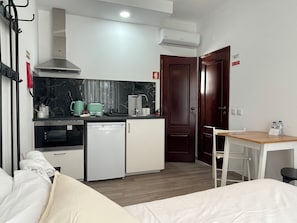 A compact hotel room with a kitchenette, a bed, a small table, and a desk.