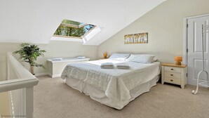 Une chambre avec un puits de lumière, un lit, des tables de chevet, une commode, une lampe, une plante et une porte.