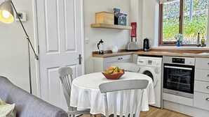 Un espace de vie compact comprenant une table et des chaises, un canapé, un lave-linge et une fenêtre donnant sur un paysage verdoyant.