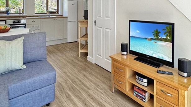 Un salon moderne avec un canapé bleu, un meuble de rangement en bois et un téléviseur diffusant une scène de plage.