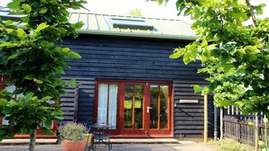 Un bâtiment en bois à l’extérieur sombre, doté de grandes portes vitrées et d’un petit espace extérieur aménagé avec une table et des chaises.
