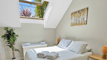 Une chambre avec un puits de lumière, un lit avec une literie blanche, une table de chevet avec une lampe et une plante en pot.