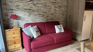 A red sofa with two decorative pillows, a wooden nightstand with drawers, a lamp, and a wooden wardrobe. - Appartement Pied des Pistes (Châtel)
