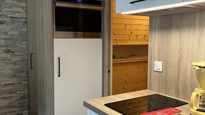 A modern kitchen with a built-in oven, a countertop with a stove, and wooden cabinetry. - Appartement Pied des Pistes (Châtel)