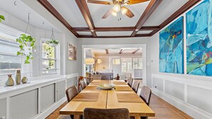 A dining room with a wooden table, chairs, hanging plants, and abstract paintings. - 1 Block to AC Beach - 8br/5ba Historic & Modern (Atlantic City)