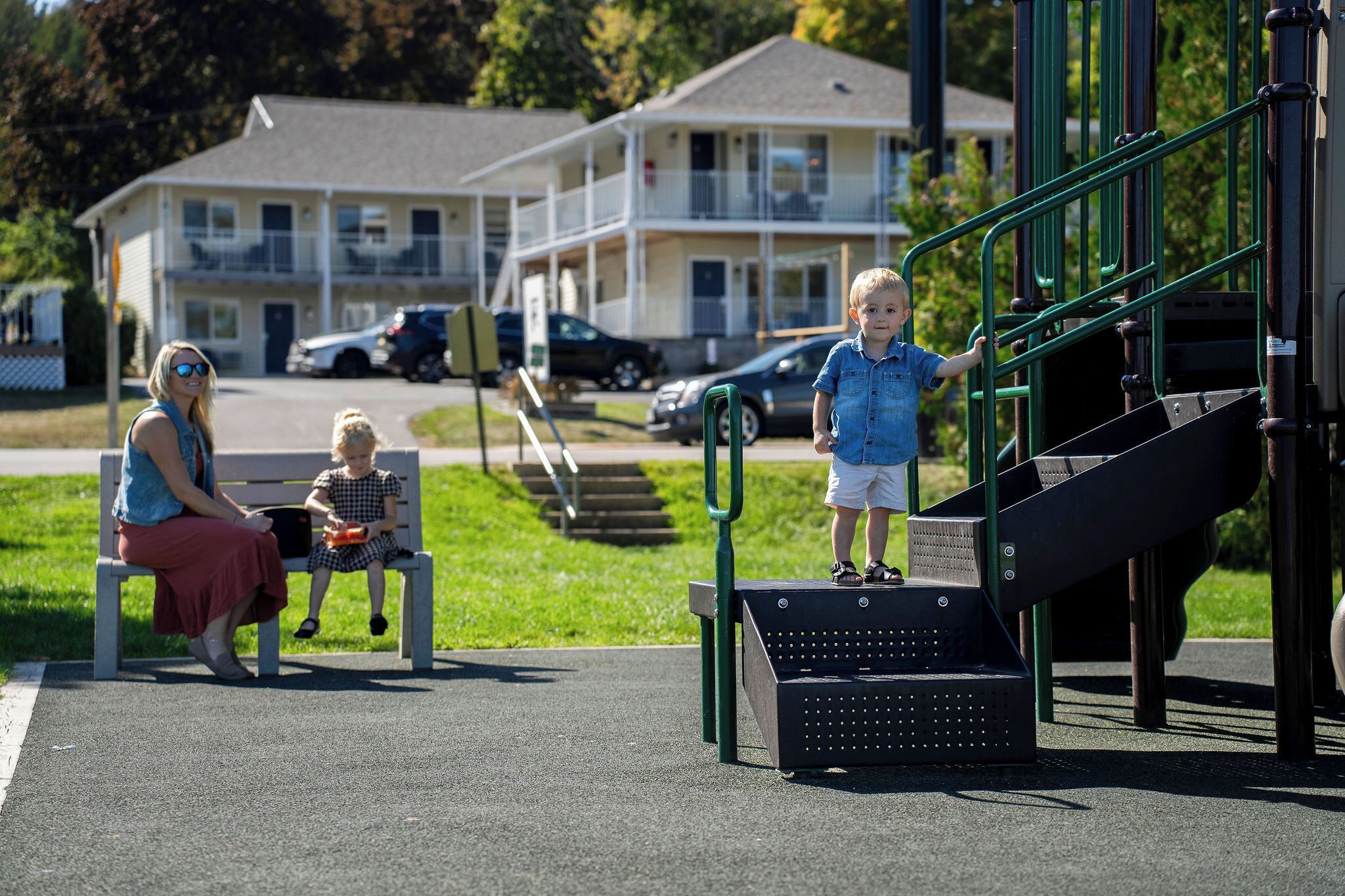 A playground with a slide and steps, a bench, and a building in the background.