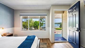 Een hotelkamer met een bed, een raam met uitzicht op een meer en een deur naar een balkon.