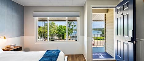 A hotel room with a bed, a window with a view of a lake, and a door leading to a balcony.