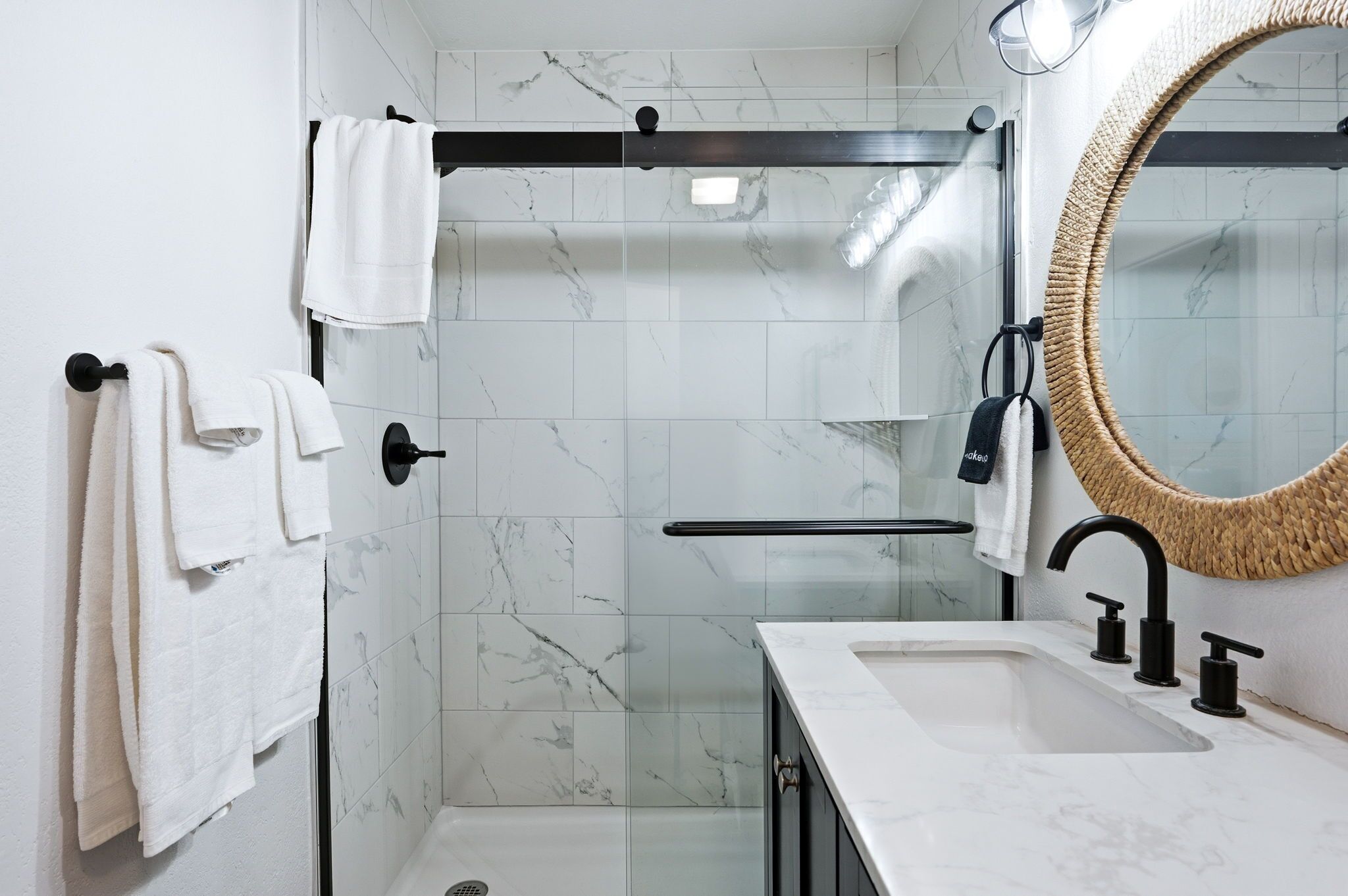 A modern bathroom with a glass-enclosed shower, a white marble sink, and a large mirror.
