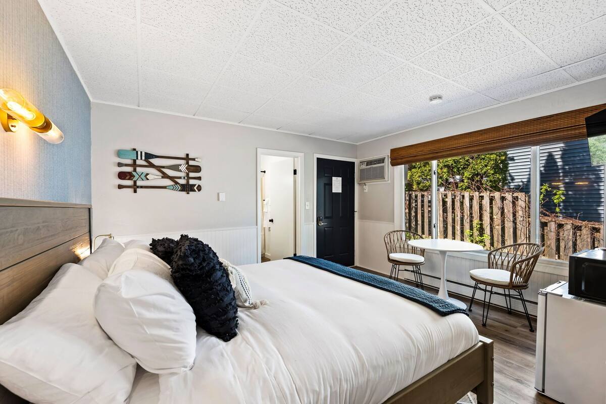 A bedroom with a bed, bedside tables, a desk, and a chair. There is a window with a view of a garden.