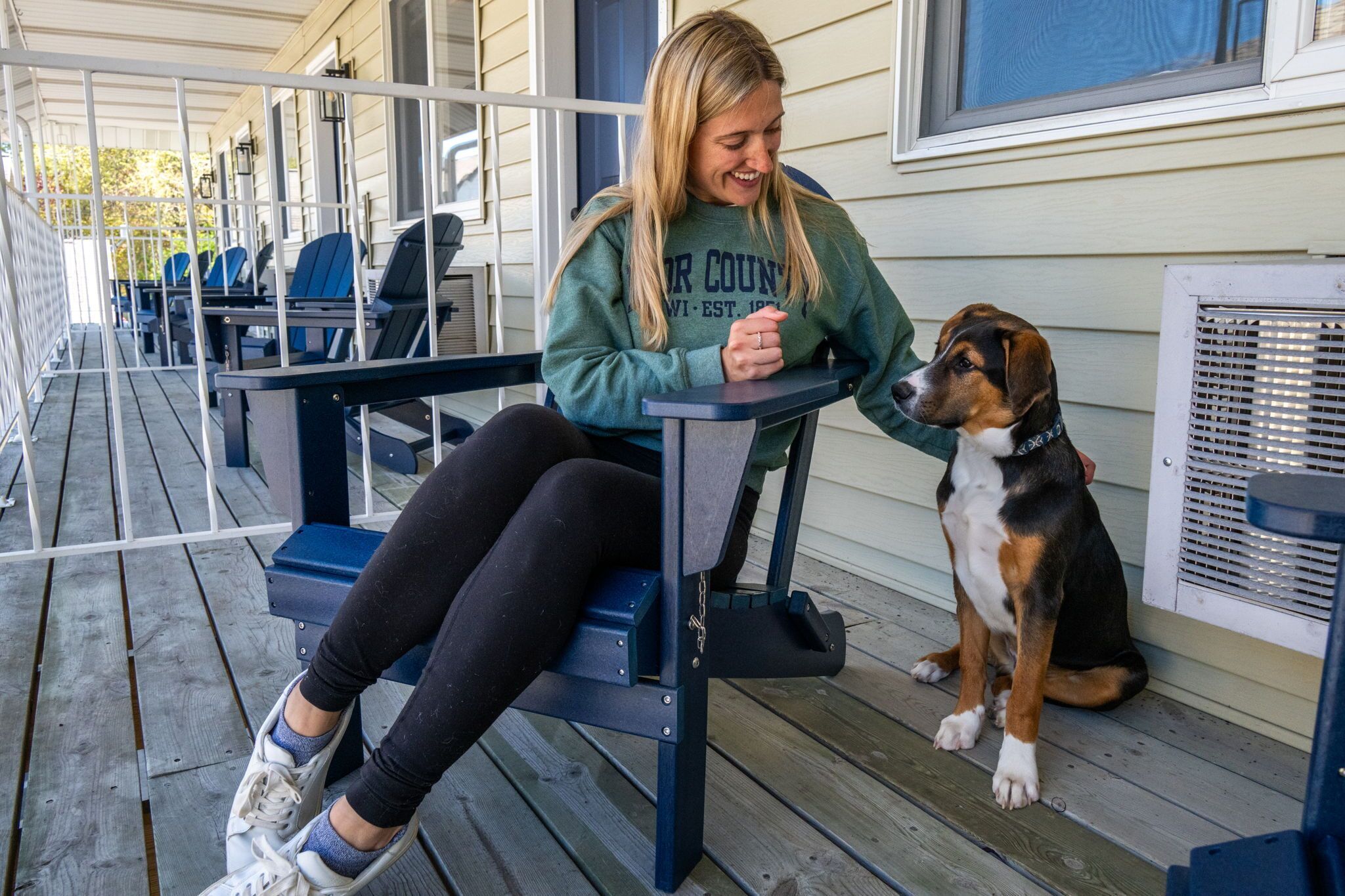 Eine Person sitzt mit einem Hund auf einer Holzterrasse auf einer Bank.