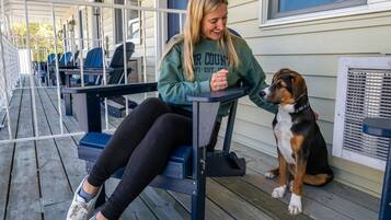 Eine Person sitzt mit einem Hund auf einer Holzterrasse auf einer Bank.