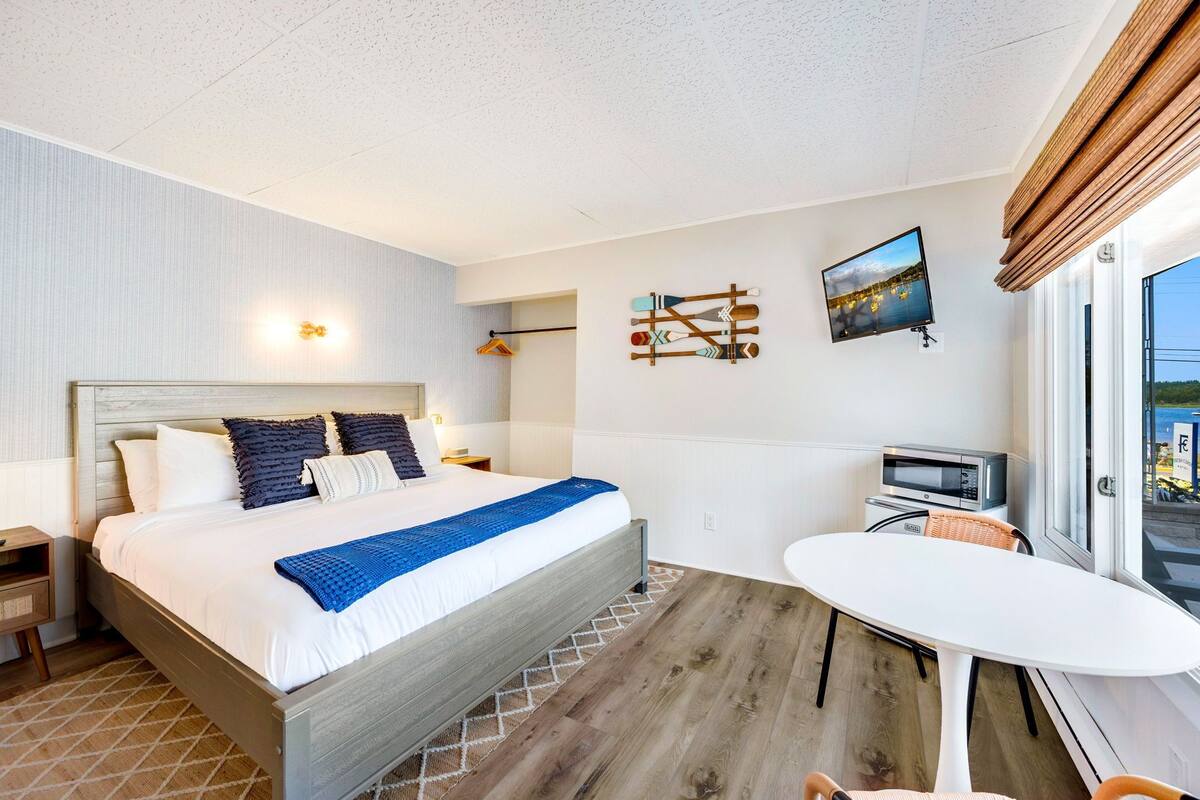 A hotel room with a bed, a dining table, a TV, and a view of the city.