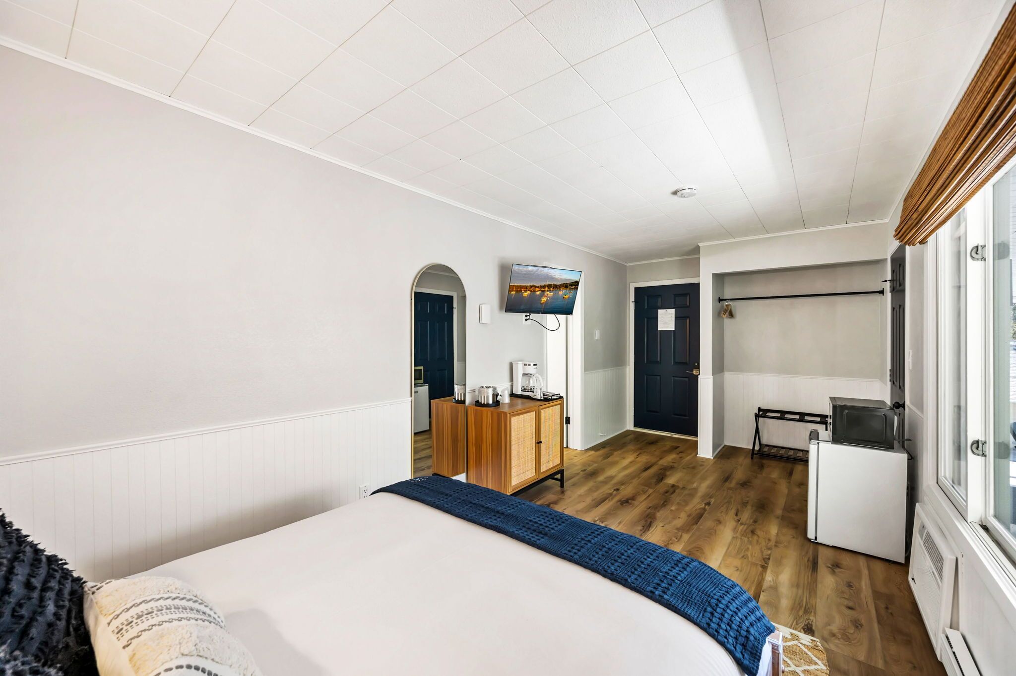 Une chambre d’hôtel équipée d’un lit, d’un bureau avec un ordinateur, d’une télévision et d’un petit réfrigérateur.