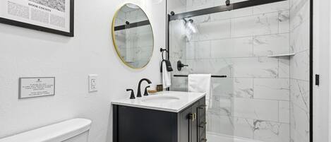 Un baño moderno con inodoro, lavamanos, espejo y ducha.
