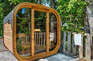 A wooden sauna structure with a glass door, surrounded by a wooden fence and trees.