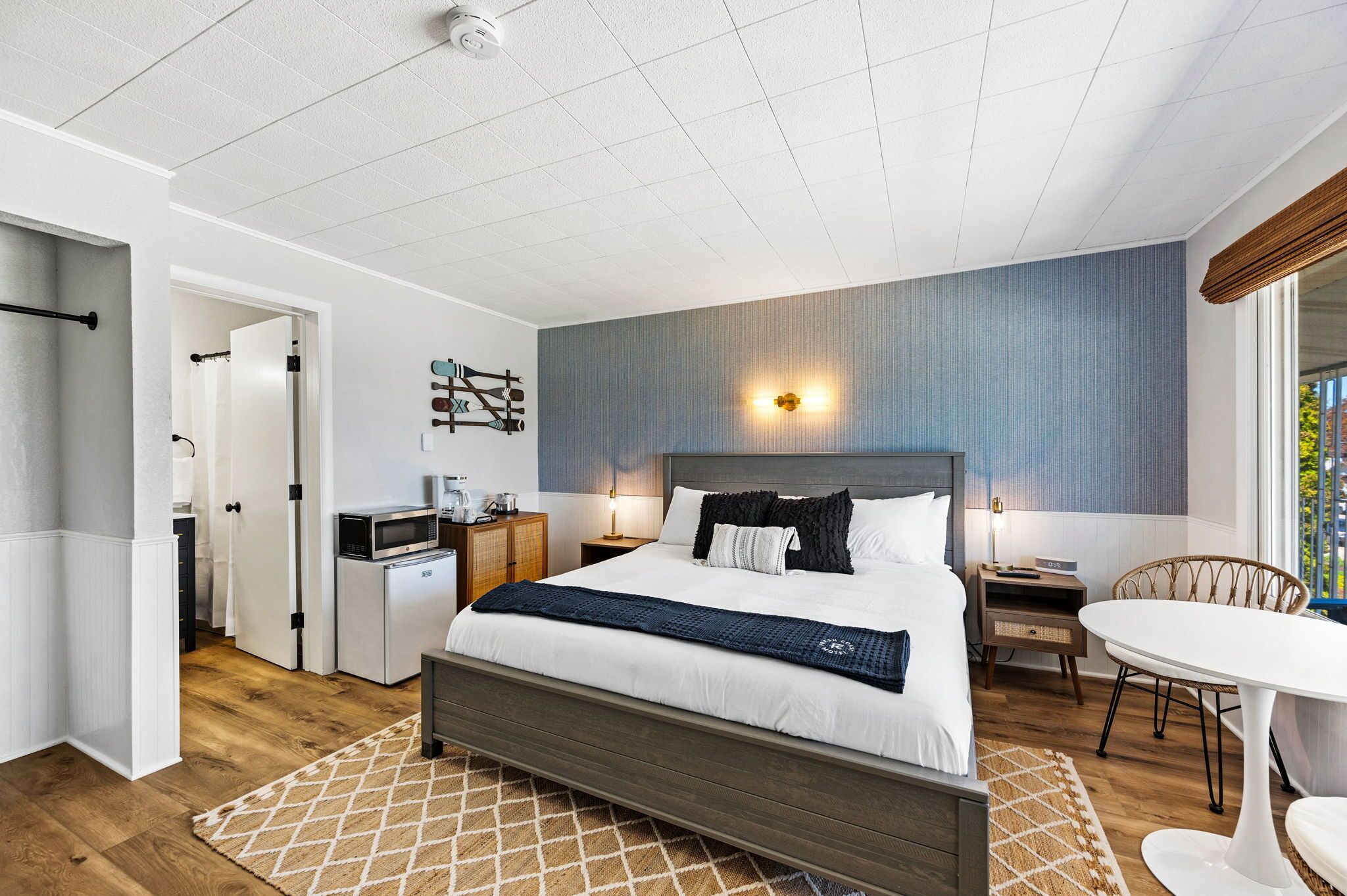 A modern bedroom with a large bed, bedside tables, a small kitchenette, and a dining area.