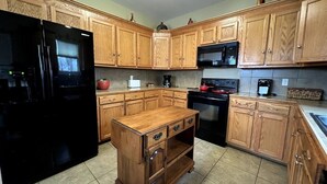 A kitchen with wooden cabinets, a black refrigerator, a microwave, and a stove. - BestStays@Bayou-Chic -work crews love us. Fenced with WIFI (Baton Rouge)