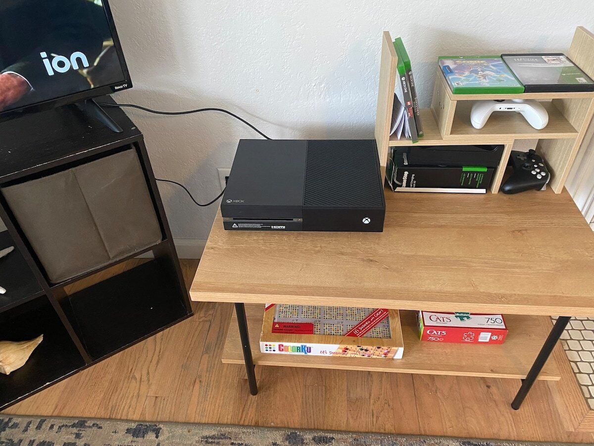 Una configuración de juego con una consola Xbox, un televisor y una mesa de madera.