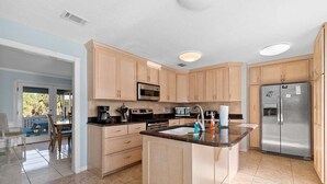 Una cocina moderna con armarios de madera clara, electrodomésticos de acero inoxidable y una isla central.
