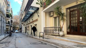 A narrow street with buildings on both sides, a man walking, and a parked motorcycle. - GK Aria by GK Hospitality Group (Athens)