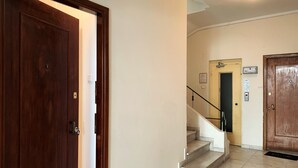 A hallway with a wooden door, a staircase, and a light fixture on the ceiling. - GK Aria by GK Hospitality Group (Athens)