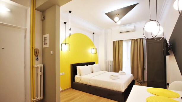A hotel room with a bed, bedside table, and a yellow accent wall. - GK Aria by GK Hospitality Group (Athens)