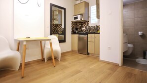 A compact kitchen with a microwave, sink, and dishwasher. There is a dining table with chairs and a mirror on the wall. The room has wooden flooring and a tiled shower area. - GK Aria by GK Hospitality Group (Athens)