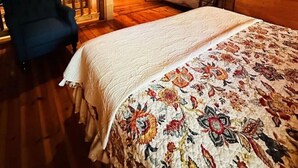 Ein gemütliches Schlafzimmer im Dachgeschoss mit Holzbalkendecke, einem Bett mit Blumenmuster, einem blauen Sessel und einer kleinen Couch.