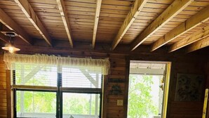 Ein Interieur einer Holzhütte mit einem gestreiften Sofa, Holzdielen und einem Fenster mit Blick auf Grünflächen.