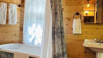 A wooden cabin bathroom with a bathtub, a sink, and a shower curtain.