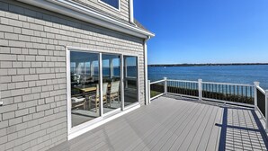Une terrasse avec vue sur l’eau, une porte vitrée donnant sur un espace patio et une rambarde blanche.