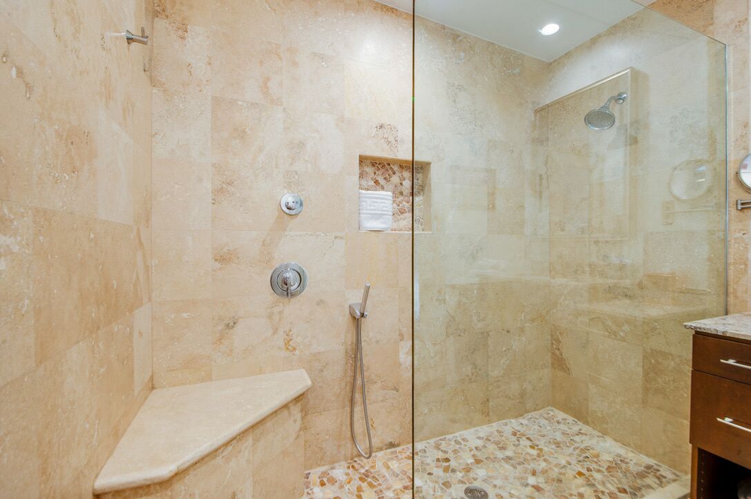 A glass-enclosed shower with beige tiles, a small shelf, and a glass door.