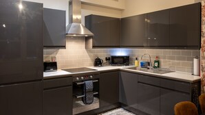 Une cuisine moderne avec des meubles de couleur sombre, une hotte de cuisinière en acier inoxydable, un four à micro-ondes et un évier équipé d’un égouttoir à vaisselle.