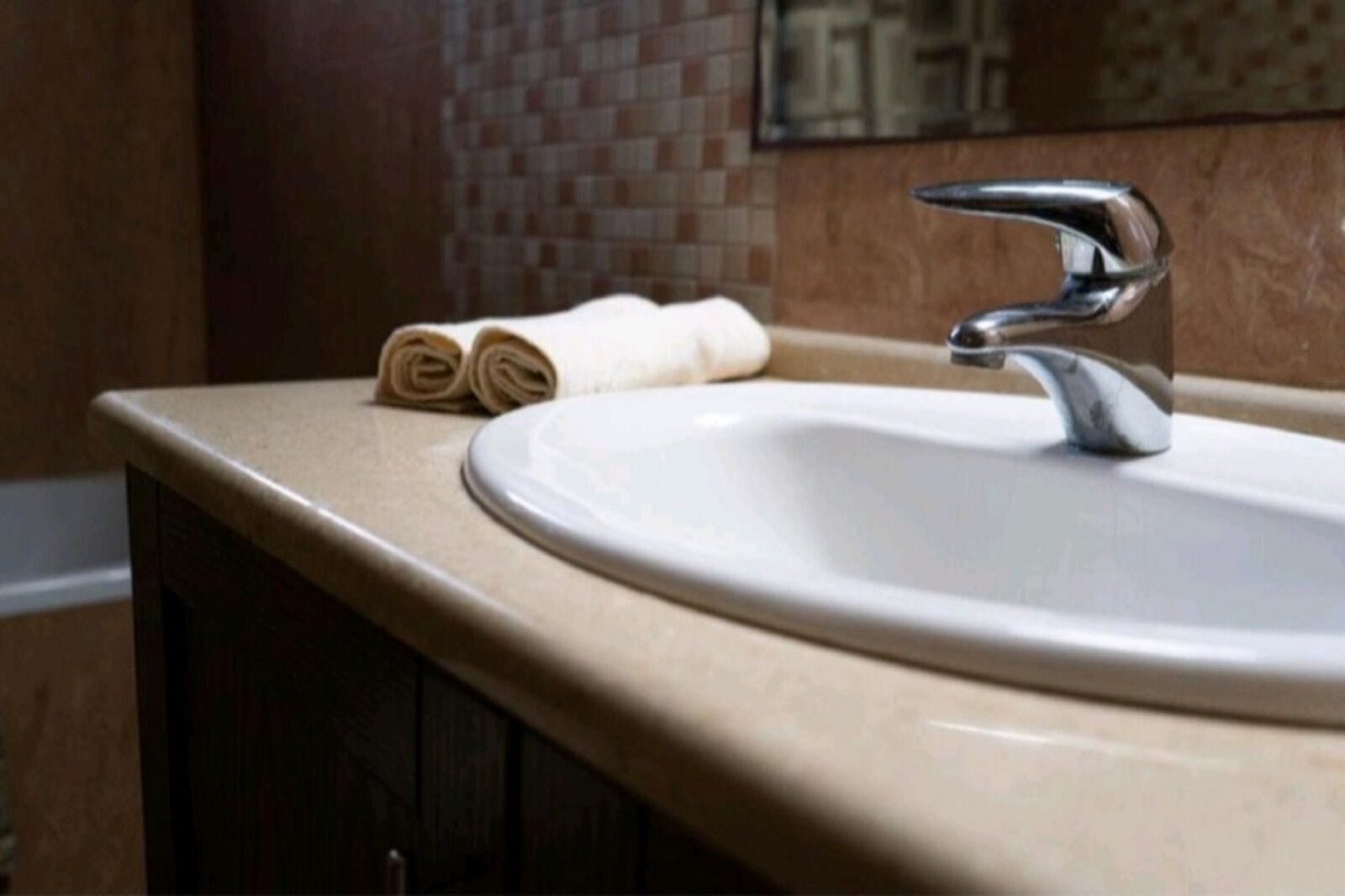 A bathroom sink with a modern faucet, a beige countertop, and a rolled towel on the counter.