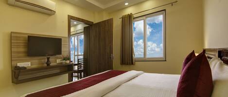 A hotel room with a bed, a TV, a desk with a chair, and a window with curtains.