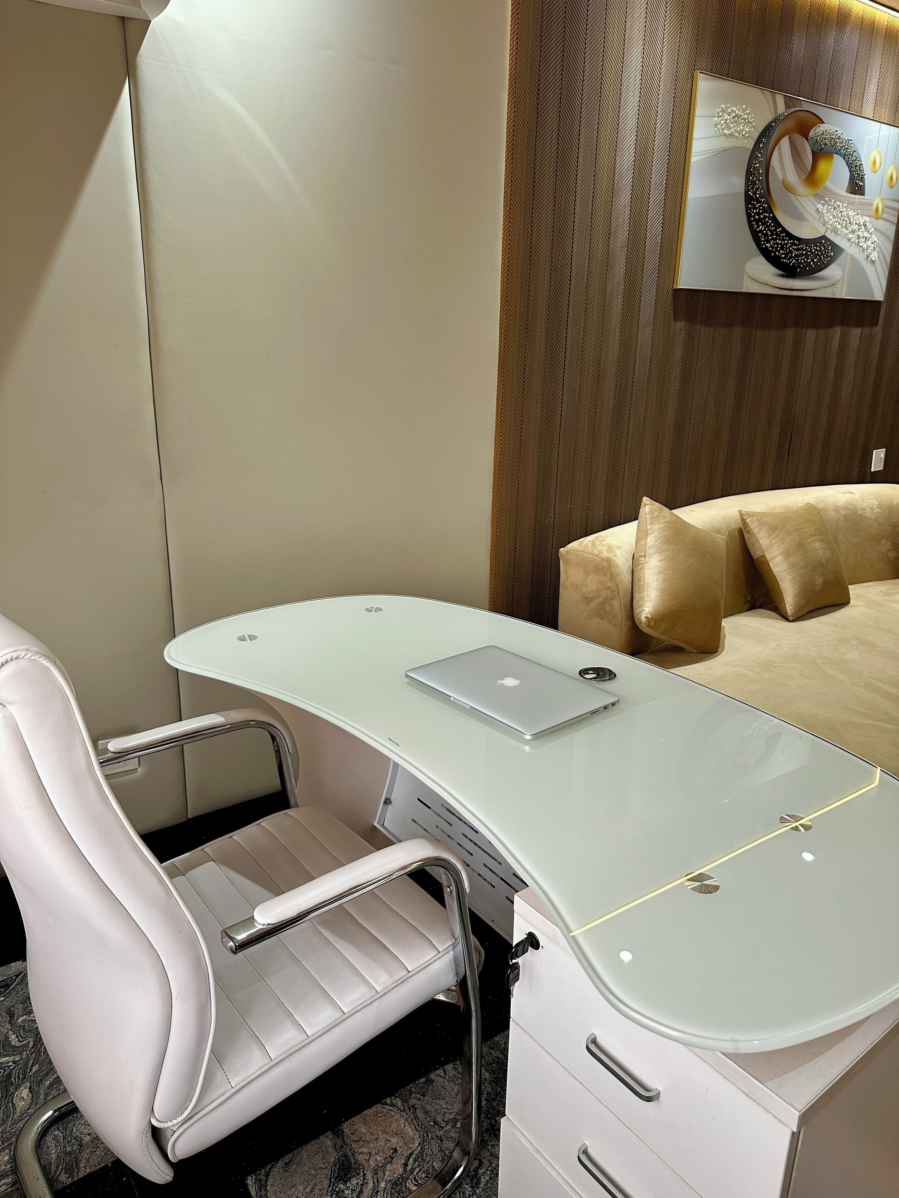 A modern office space with a white desk, a laptop, a white chair, and a beige sofa.